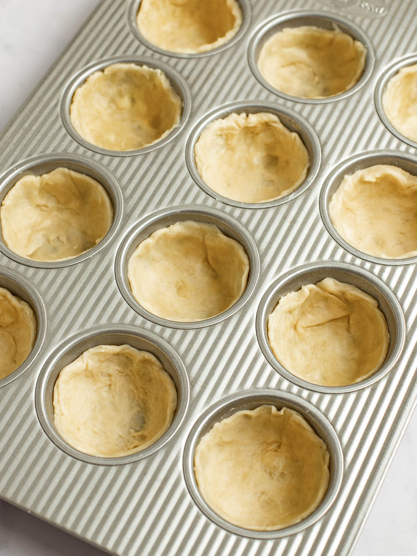 Circular pieces of pie crust pressed into a muffin pan.