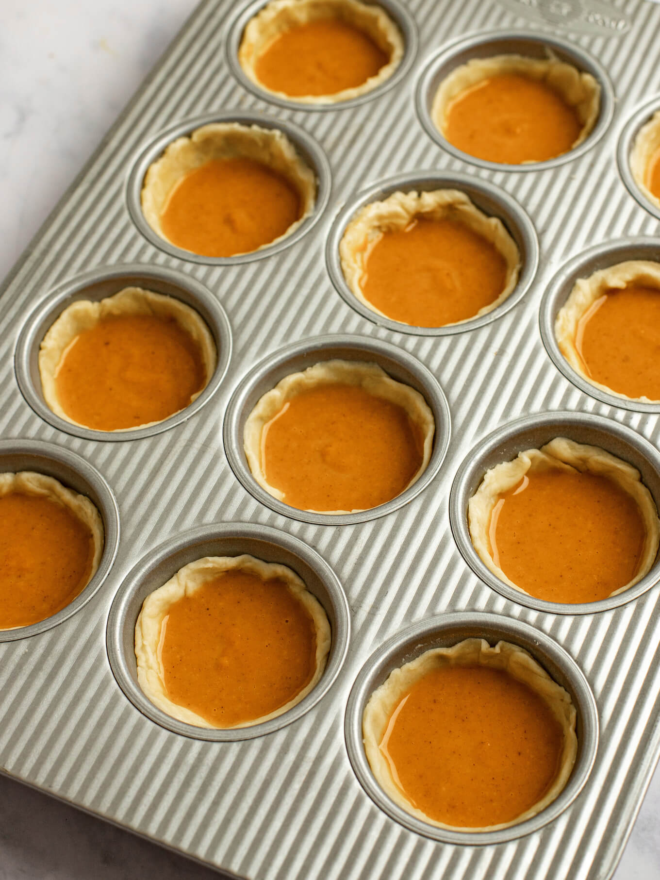 Pumpkin pie filling added to the pie crusts in the muffin pan.