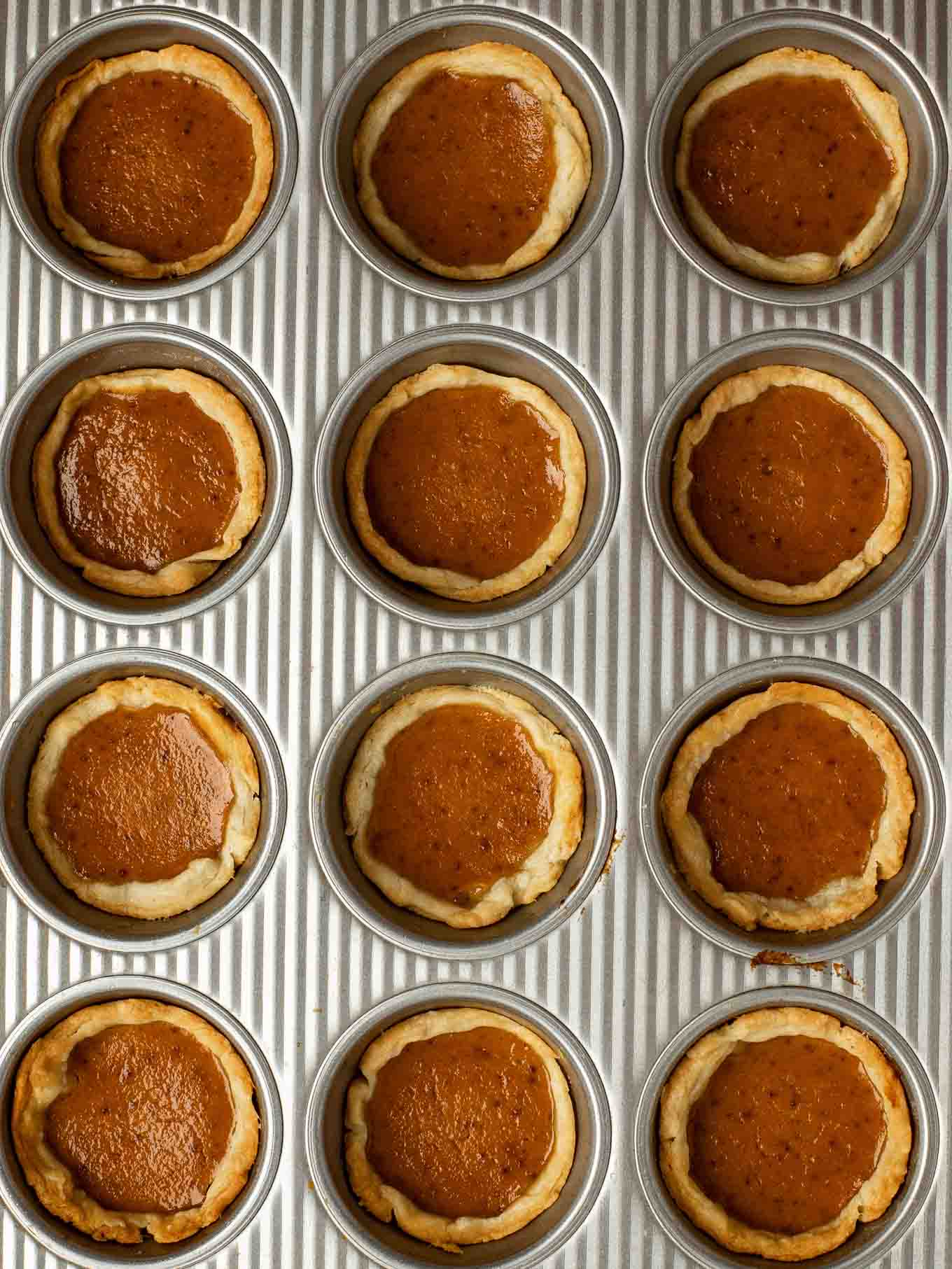 An overhead view of baked mini pumpkin pies in a muffin pan.