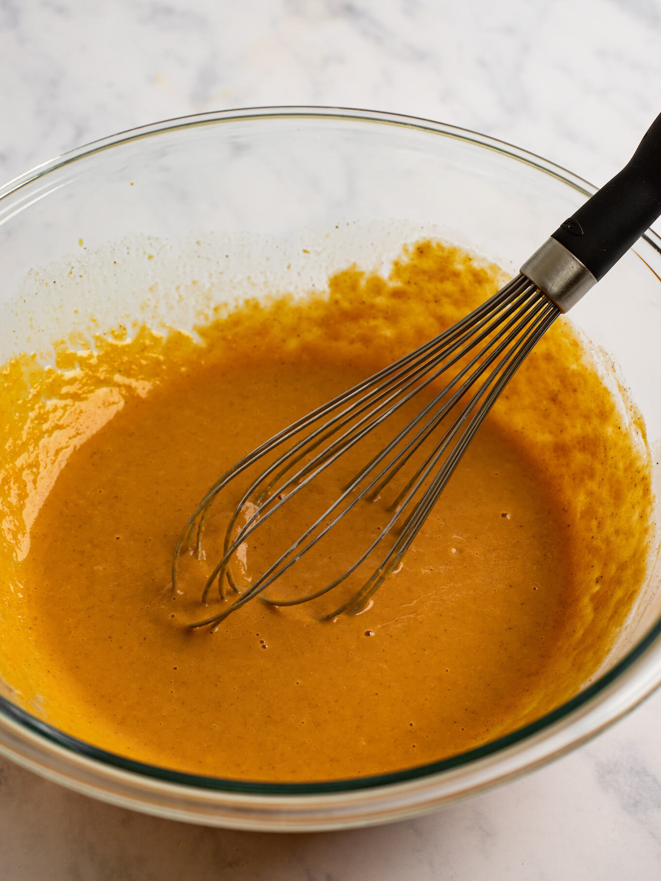 The filling ingredients whisked together in a glass mixing bowl. A whisk rests on the side of the bowl.