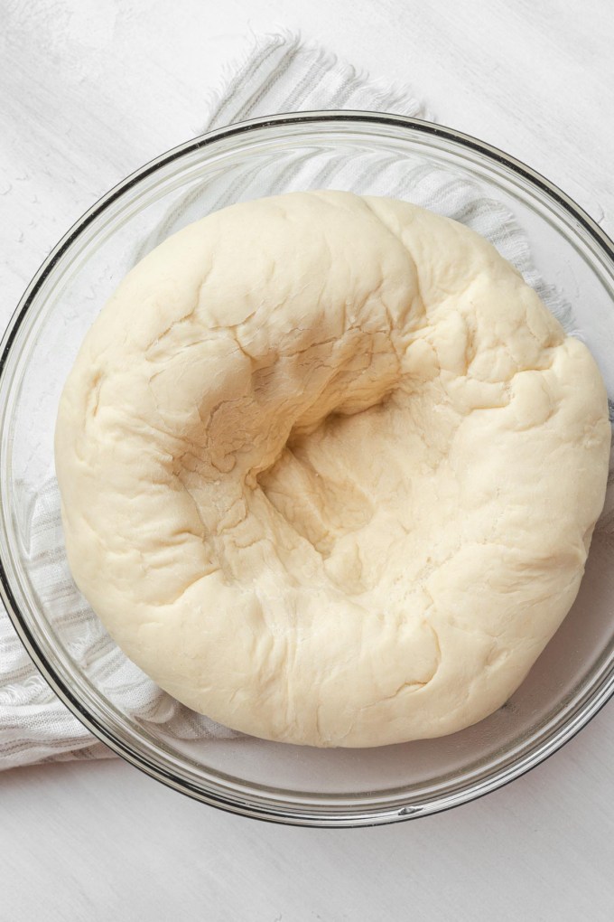 An overhead view of bread dough that's been punched down in a glass mixing bowl.