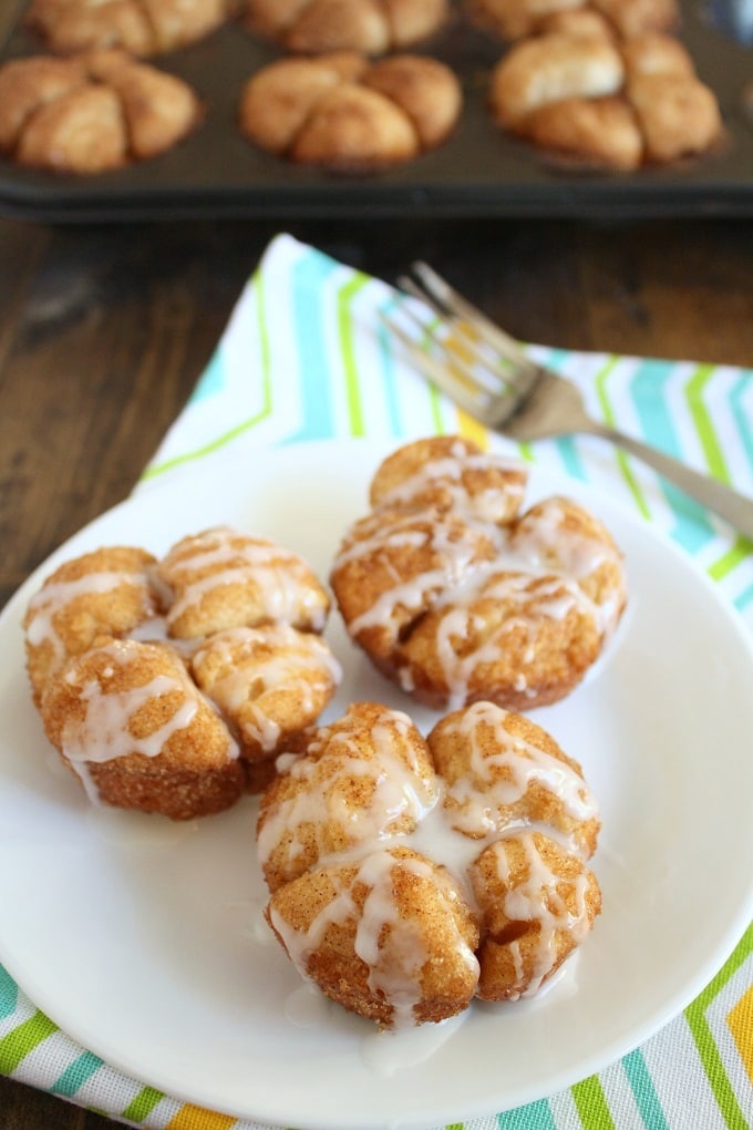 Three pull apart Monkey Bread Muffins on a white plate. A pan of muffins rests in the background. 