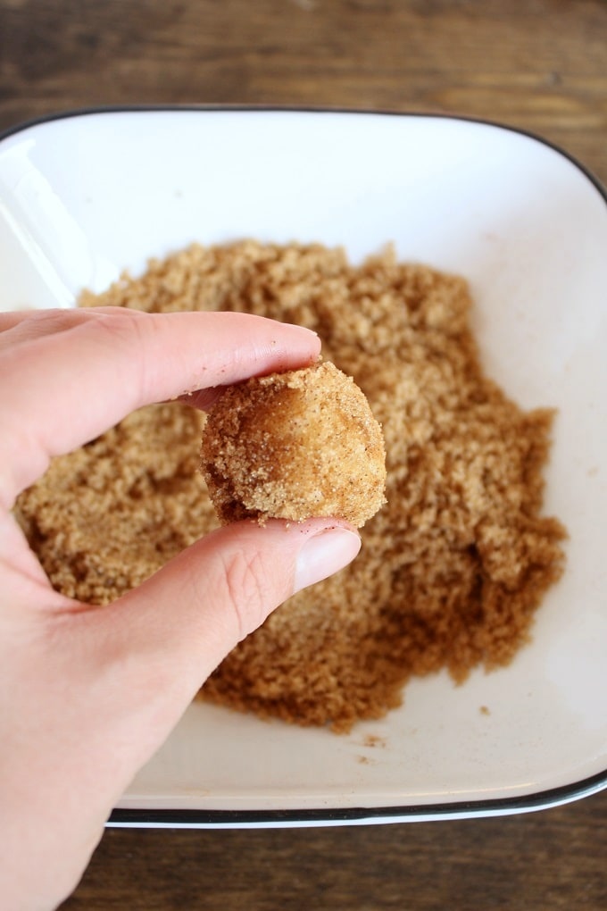 A ball of raw dough coated in cinnamon-sugar being held aloft. 