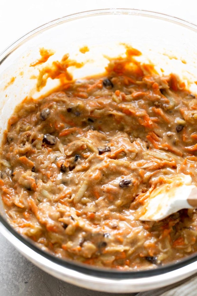 Morning glory muffin batter in a glass mixing bowl. A rubber spatula rests on top of the batter.