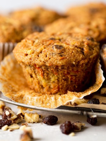 Side view of morning glory muffins on a wire cooling rack. The front muffin has had the paper liner pulled down.