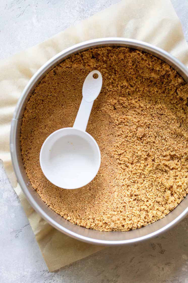 A springform pan holding graham cracker crumbs being pressed down for the crust.