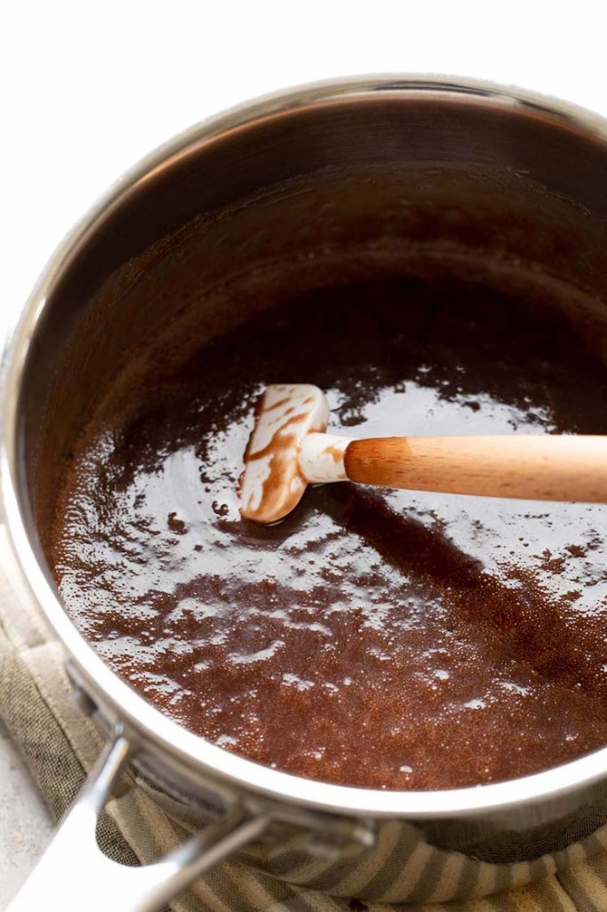 The butter, sugar, milk, and cocoa powder in a large saucepan after it's been melted together and boiled for one minute. A rubber spatula rests inside the saucepan.
