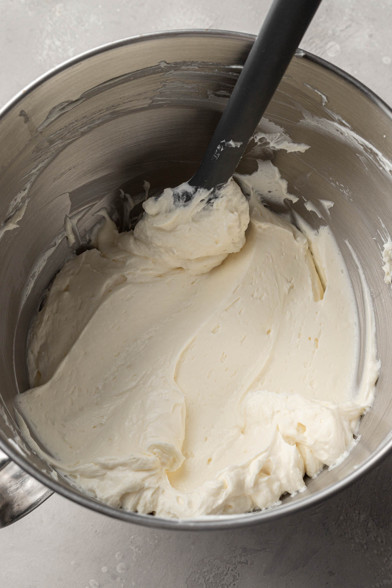 An overhead view of the cheesecake mixture in a mixing bowl, with a rubber spatula. 