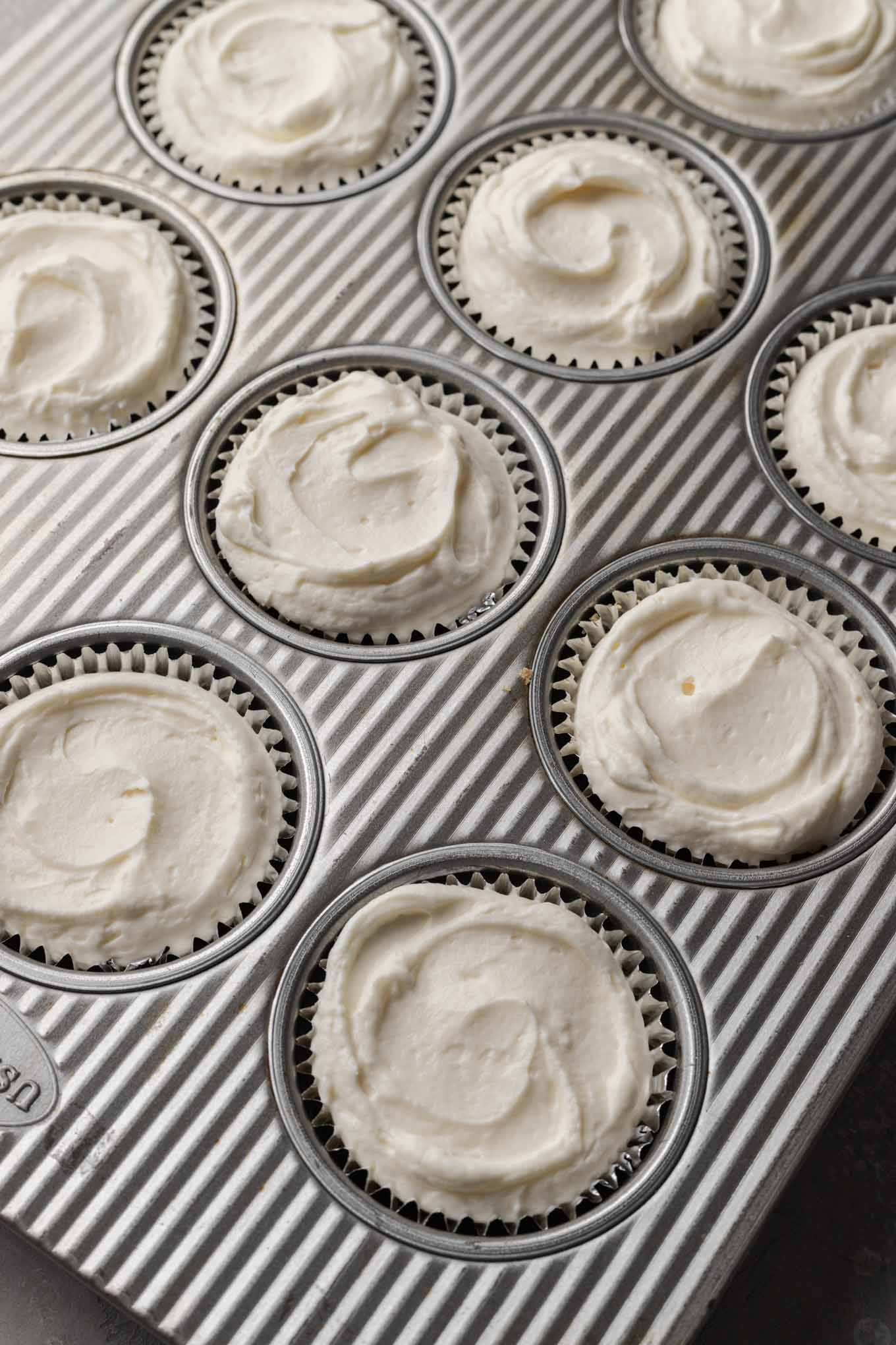 An overhead view of muffin cups filled with cheesecake filling. 