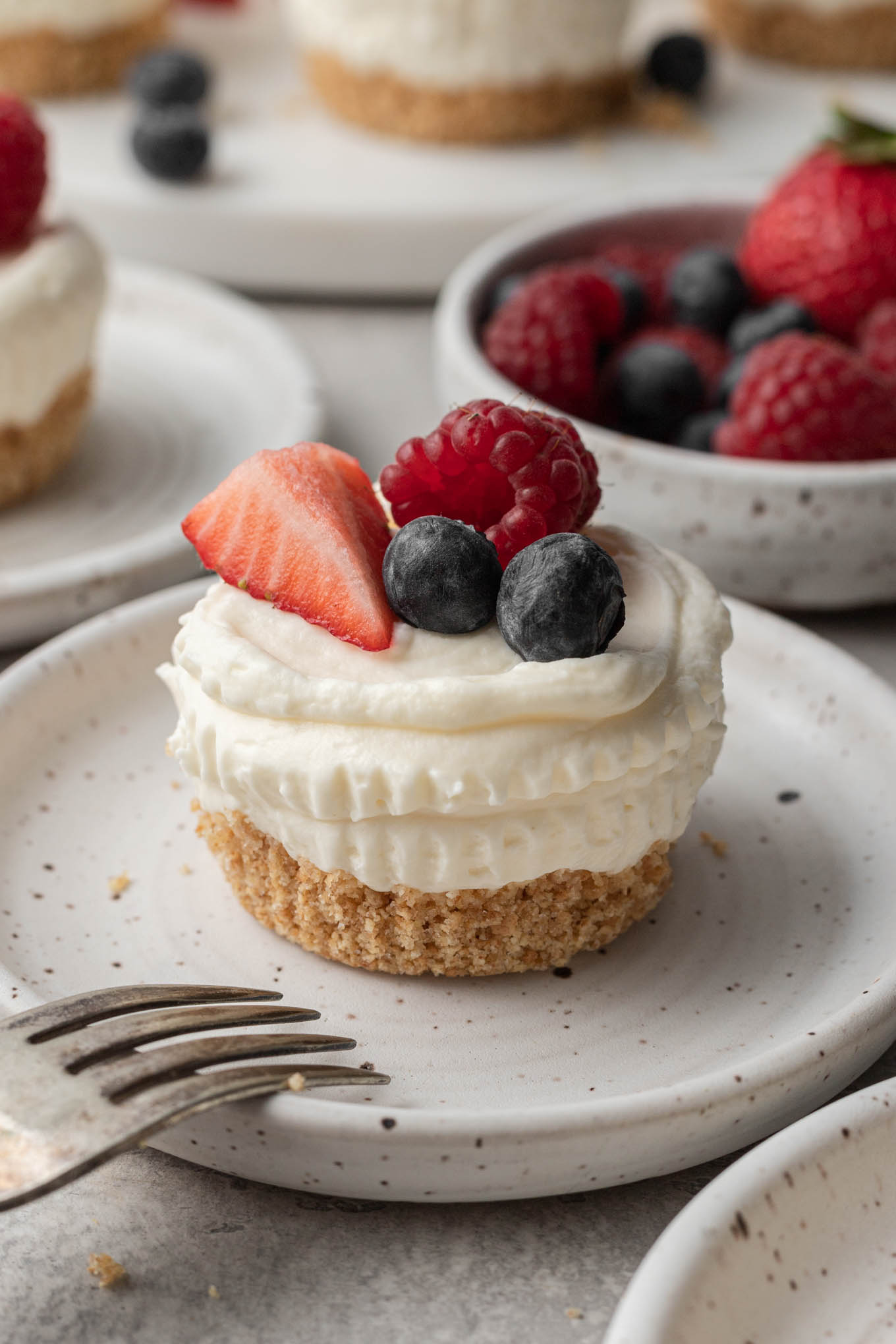 A no bake mini cheesecake topped with fresh berries, on a speckled white dessert plate. 