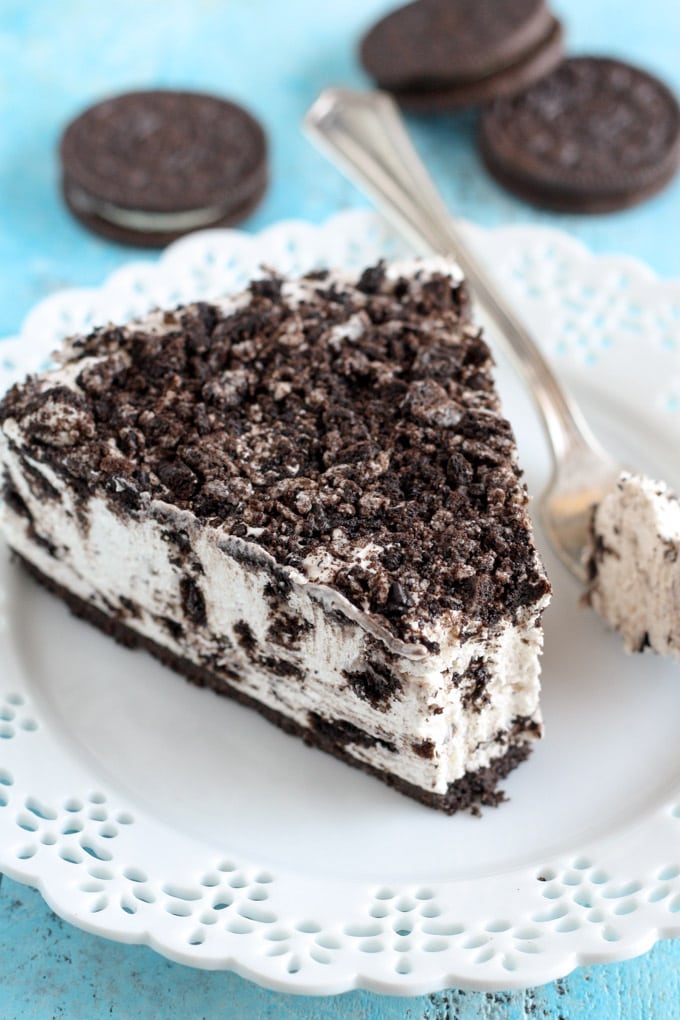 A slice of no-bake Oreo cheesecake on a white plate. Three Oreos rest in the background. 