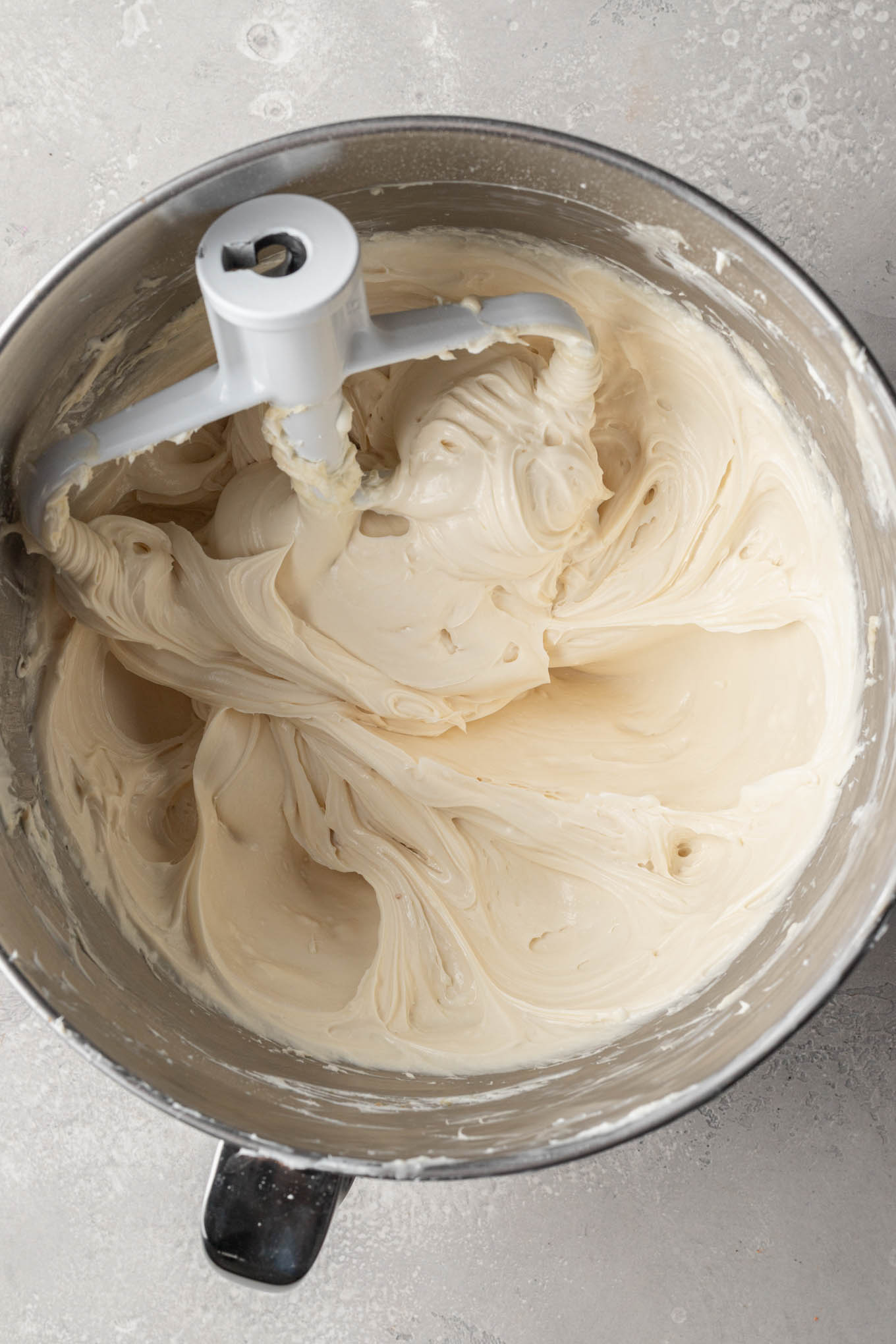 An overhead view of a cream cheese mixture in the bowl of a stand mixer, with a paddle attachment. 