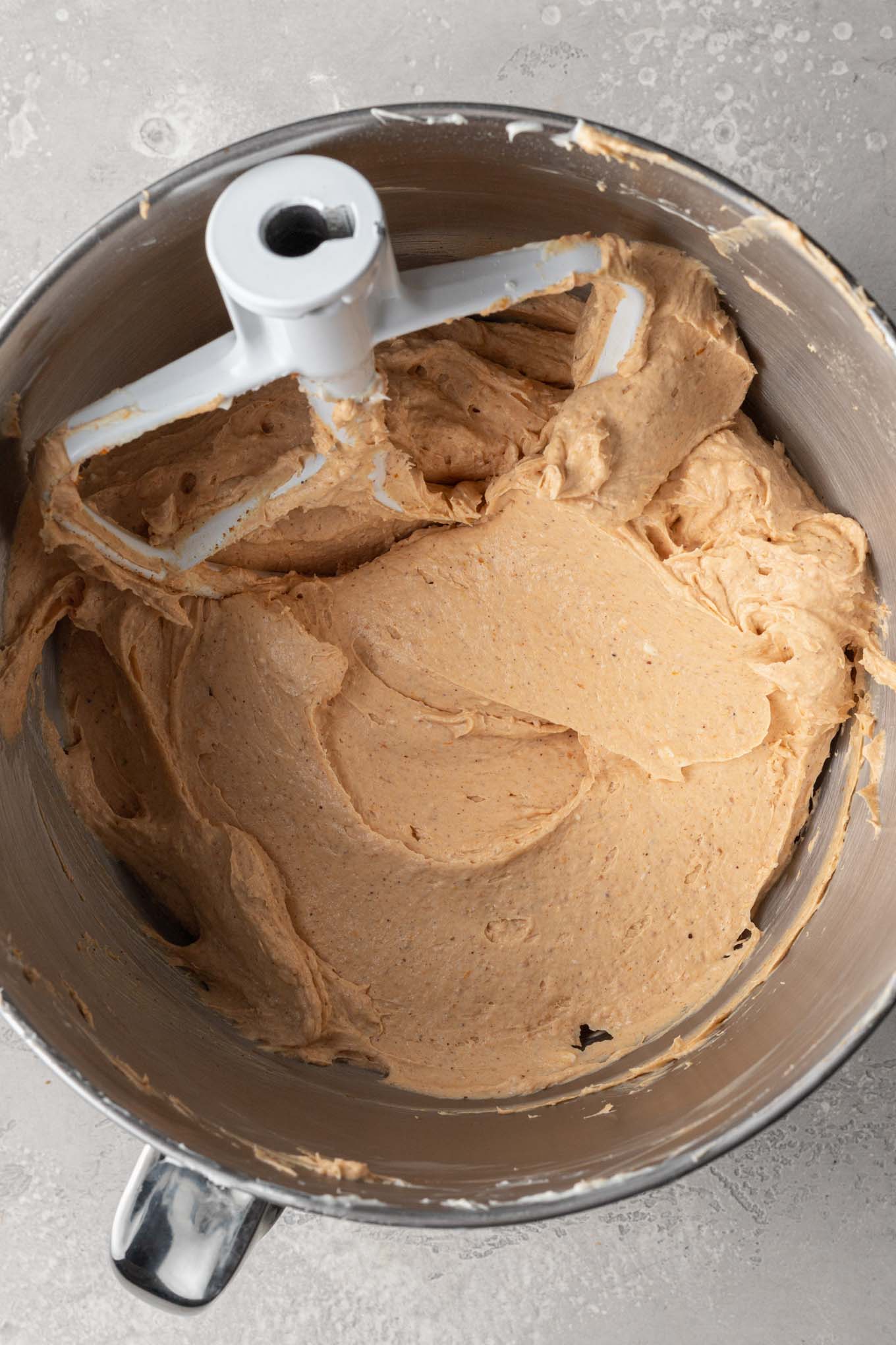 An overhead view of no bake pumpkin cheesecake filling in the bowl of a stand mixer, with a paddle attachment. 