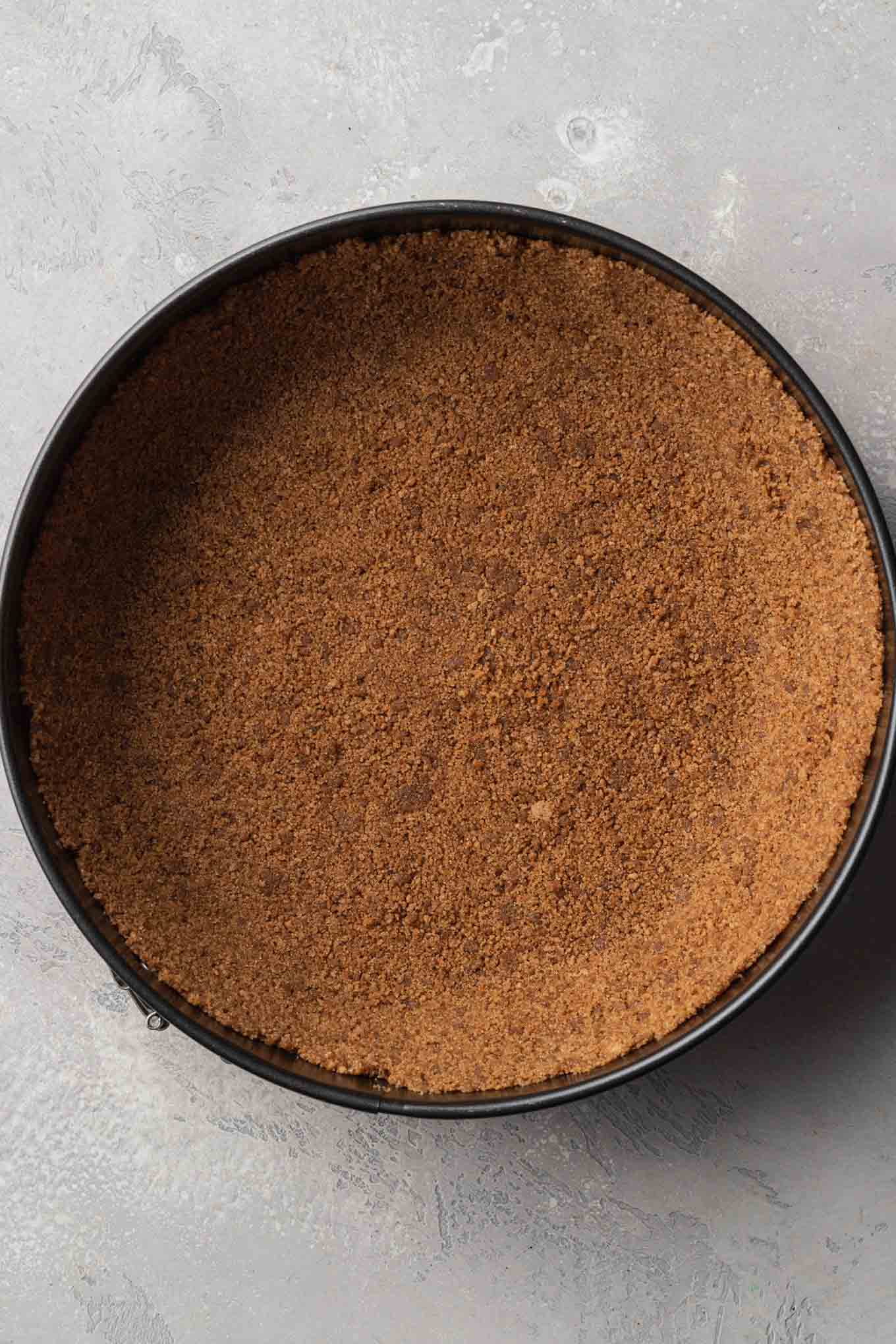 An overhead view of a gingersnap cookie crust in a springform pan. 