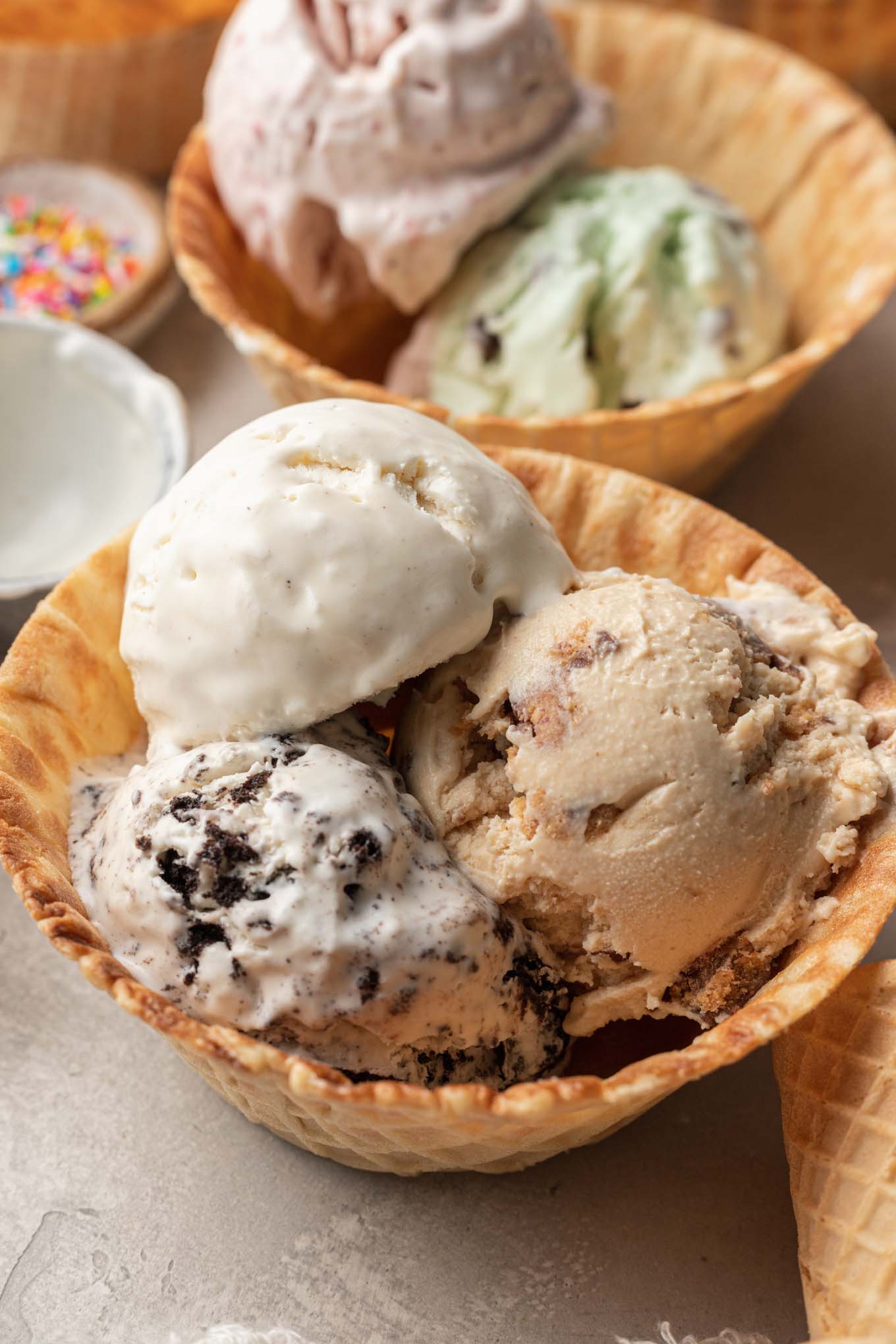 Two waffle cone bowls filled with scoops of homemade no churn ice cream of various flavors. 