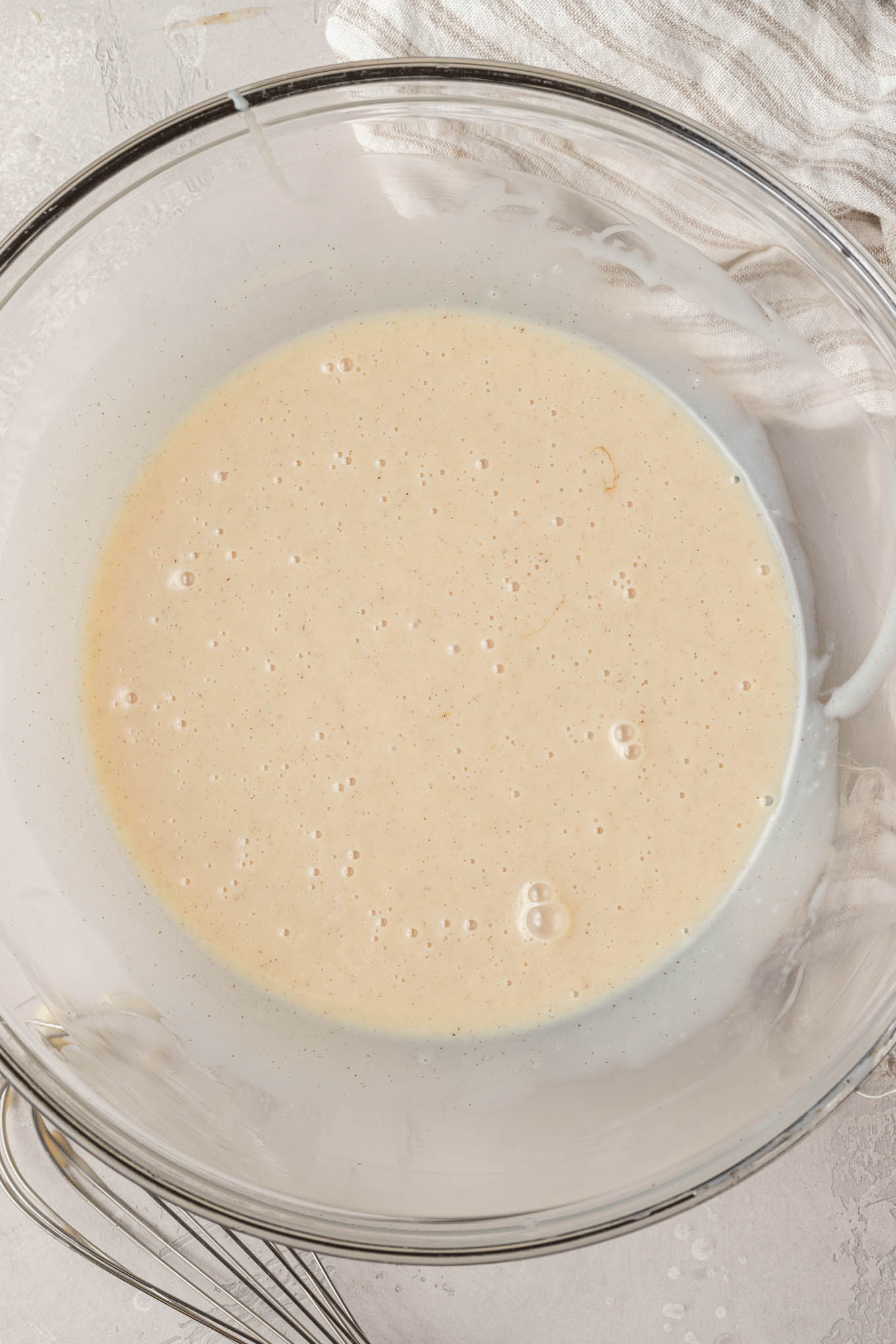 An overhead view of sweetened condensed milk, vanilla extract, and salt whisked together in a glass mixing bowl.