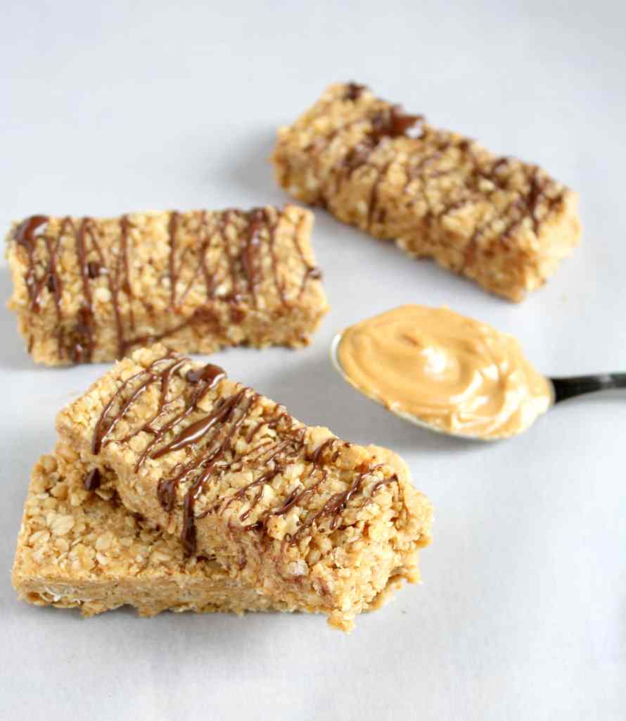 Four no bake peanut butter granola bars drizzled with chocolate. A spoonful of peanut butter rests nearby. 