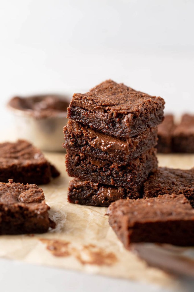 A stack of four brownies, with additional brownies scattered around. 