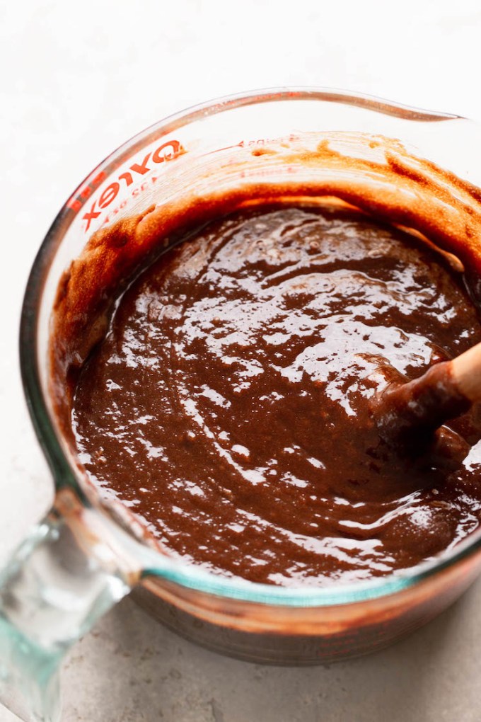 An overhead view of brownie batter in a glass bowl with a spoon.