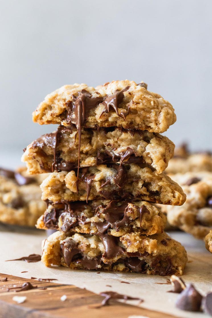 A stack of oatmeal chocolate chip cookies cut in half and melted chocolate running down the front of them.