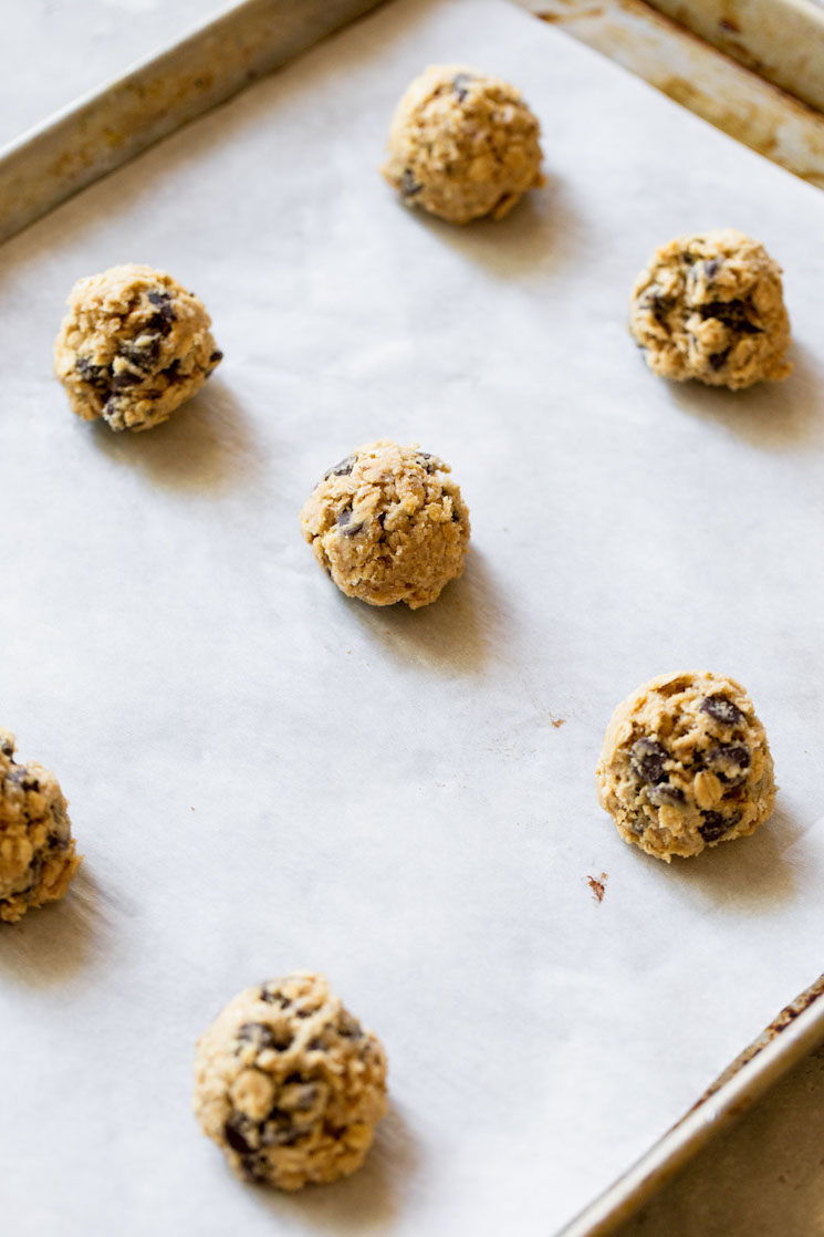 An antique baking sheet lined with parchment paper holding balls of oatmeal chocolate chip cookie dough ready to be baked.