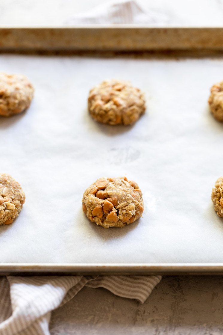 An antique baking pan lined with parchment paper with slightly flattened cookie dough ready to go into the oven.