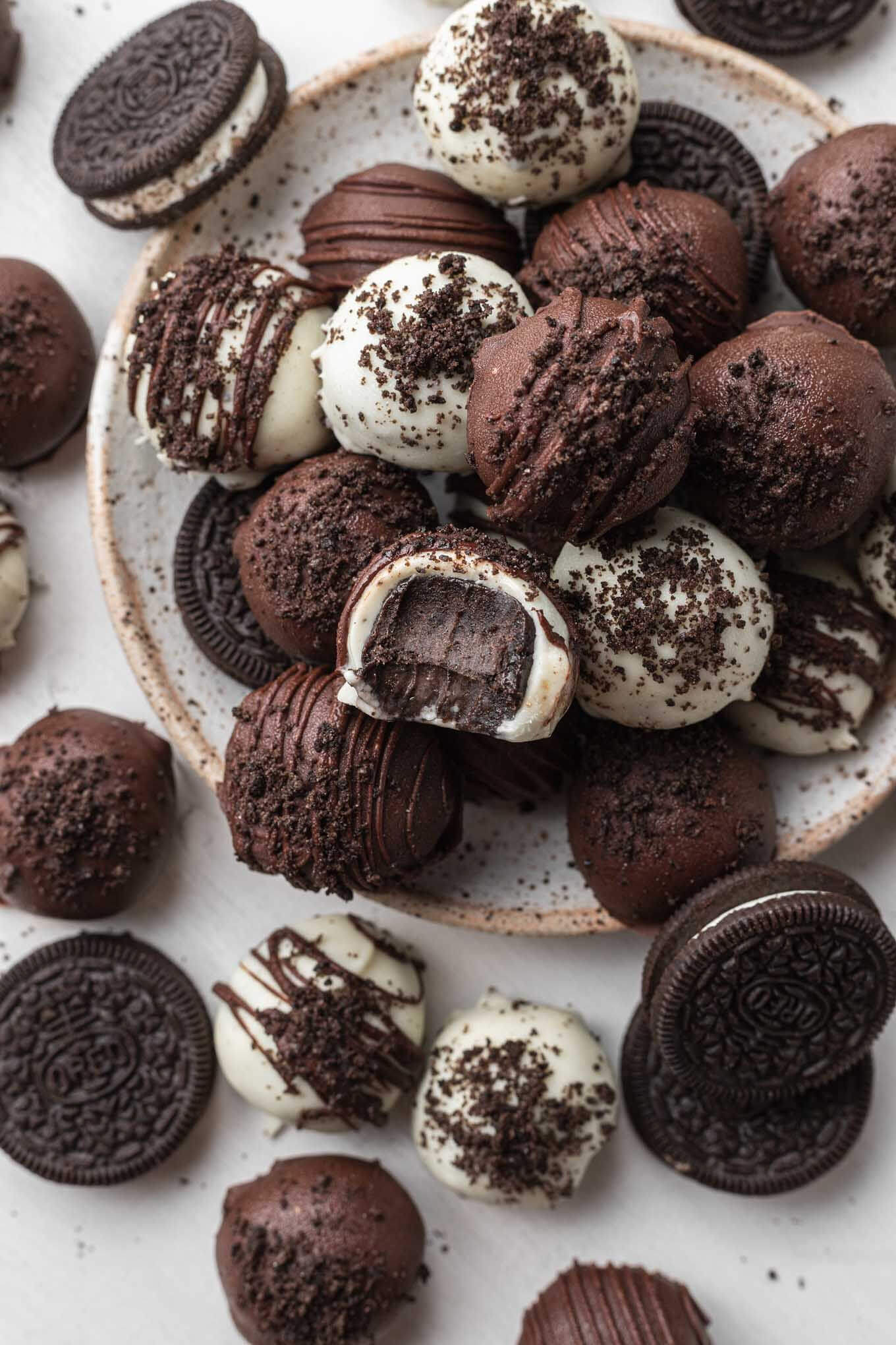 An overhead view of a stack of Oreo cream cheese balls on a speckled white plate. One ball has a bite missing. 