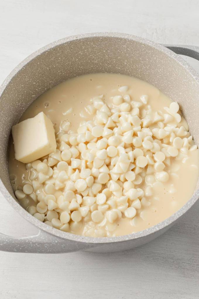 An overhead view of white chocolate chips, butter, and sweetened condensed milk in a saucepan.