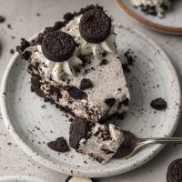 A slice of Oreo pie on a white speckled plate. A fork with a piece of the pie rests on the plate.