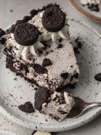 A slice of Oreo pie on a white speckled plate. A fork with a piece of the pie rests on the plate.