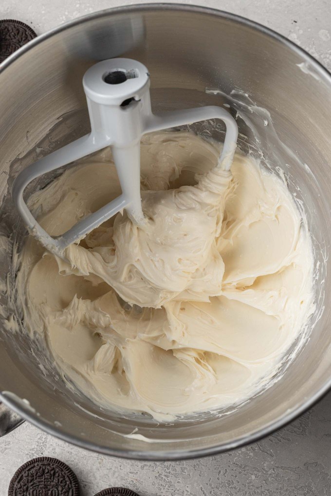 An overhead view of cream cheese, powdered sugar, and vanilla extract mixed together in the bowl of a stand mixer.