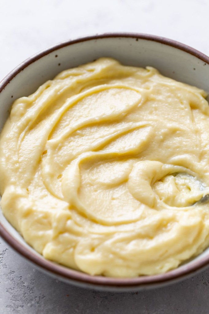 Vanilla pastry cream that's been chilled and allowed to set. The pastry cream is in a speckled white bowl. 