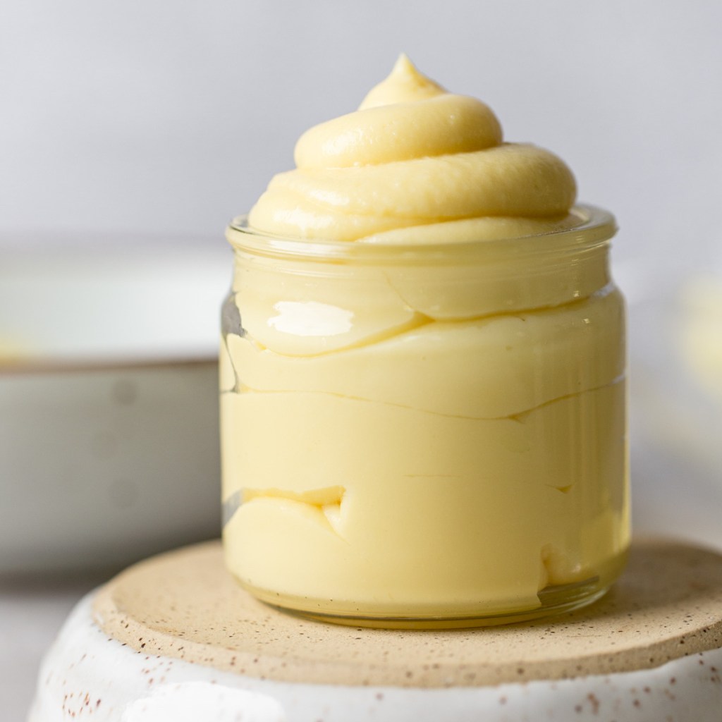 A straight on image of pastry cream in a glass jar. The jar is sitting on top of an overturned bowl.