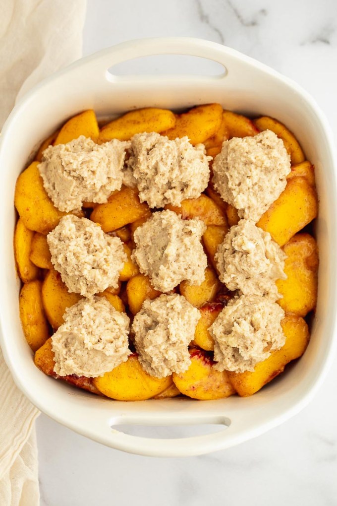 A white baking dish filled with peach filling and topped with a biscuit topping.