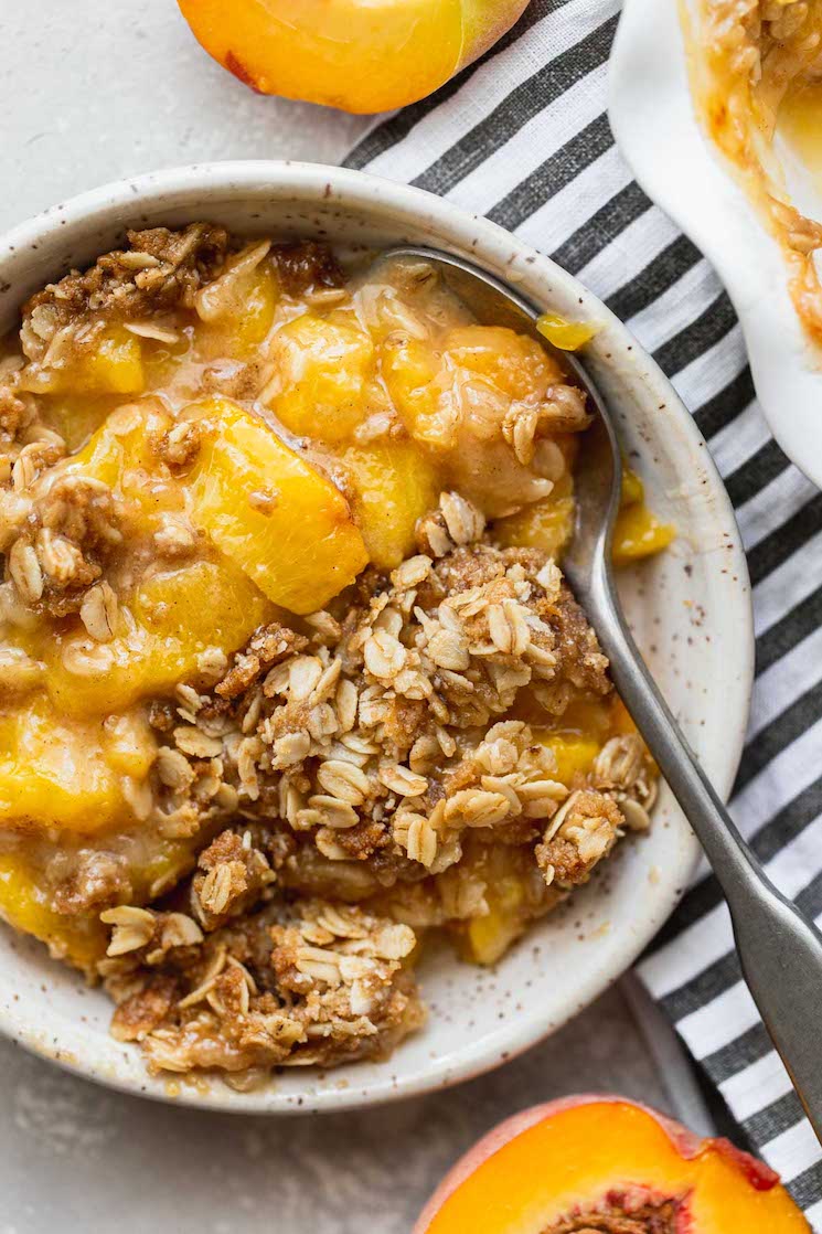 A serving of peach crisp in a white bowl with a spoon in it.