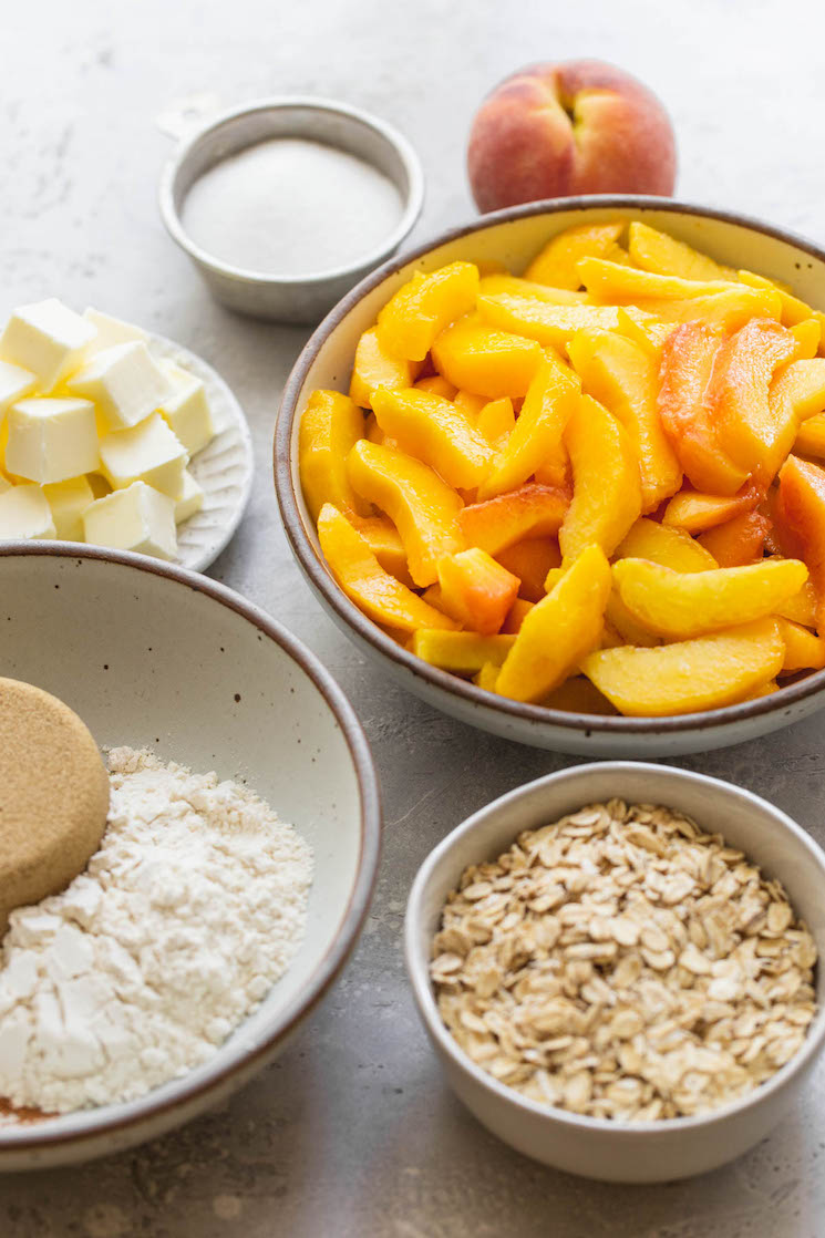 The ingredients needed to make peach crisp in various bowls on a gray surface.