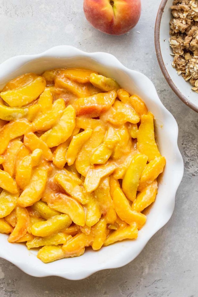 Sliced peaches in a round baking dish ready to be topped with the oat topping.