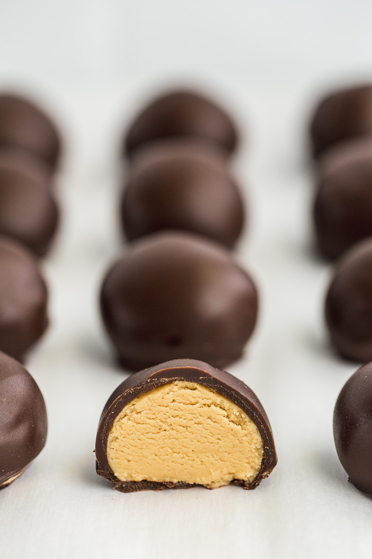 A baking sheet filled with finished peanut butter balls and one cut in half to show the inside. 