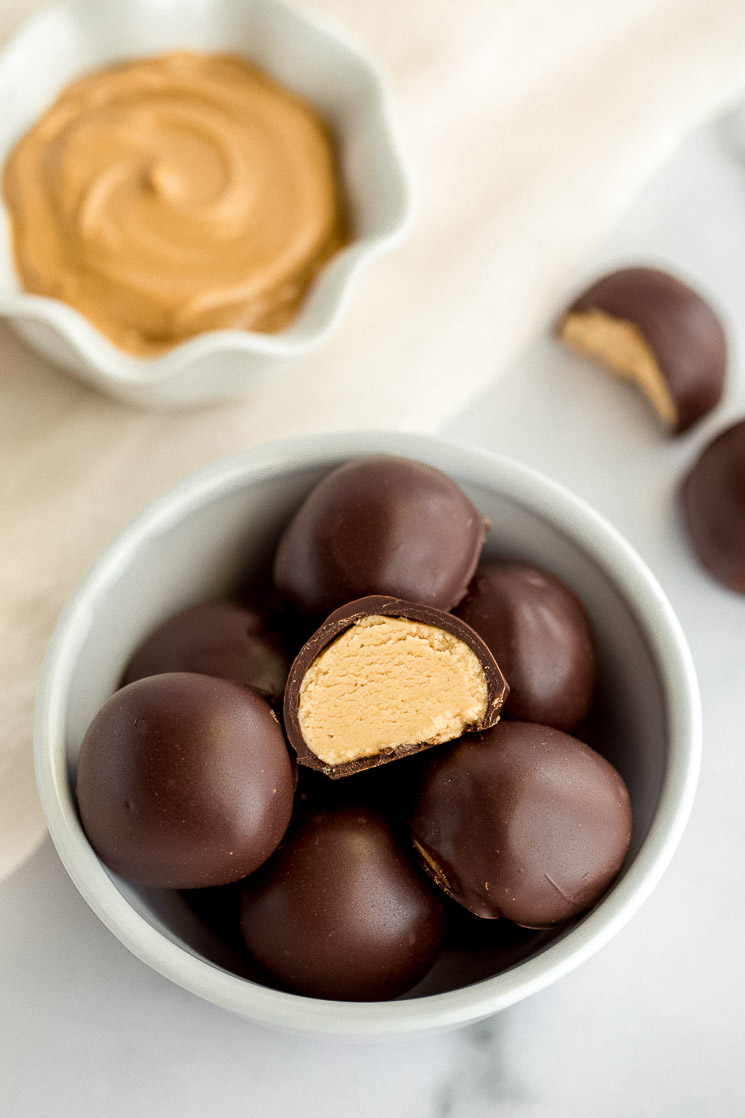 A white bowl filled with peanut butter balls and a small bowl of peanut butter in the background. 