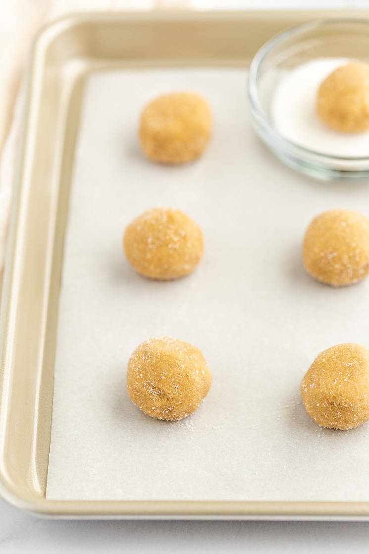 A baking sheet lined with parchment paper and cookie dough balls covered in sugar on the pan.