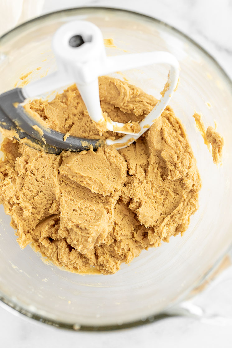 A glass mixing bowl with peanut butter cookie dough with the beater still in it.