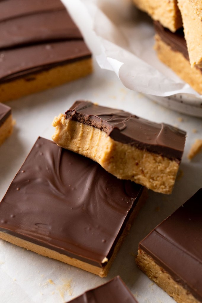 A chocolate peanut butter candy bar with a bite missing resting atop another bar. 