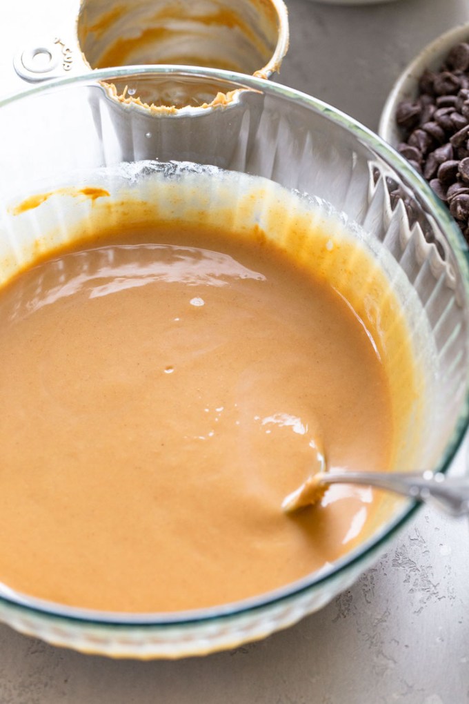 Peanut butter and melted butter whisked together in a large glass bowl. A spoon rests inside the bowl.