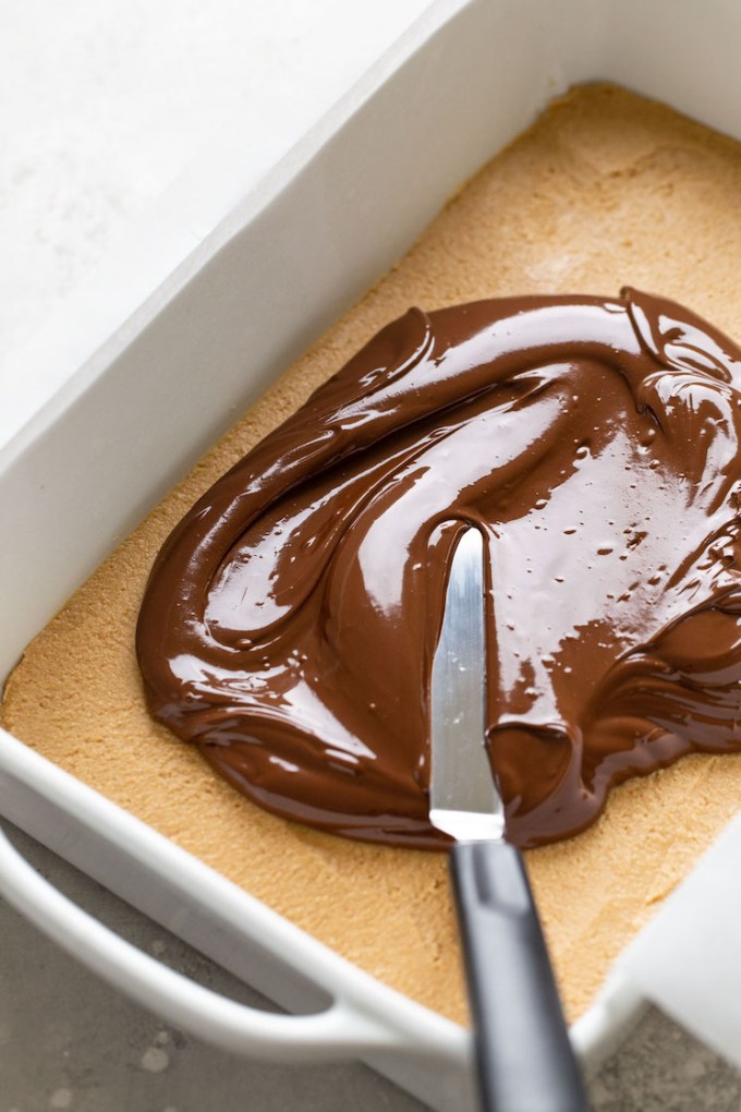 A chocolate-peanut butter mixture being spread over a firm peanut butter base in a large baking dish.