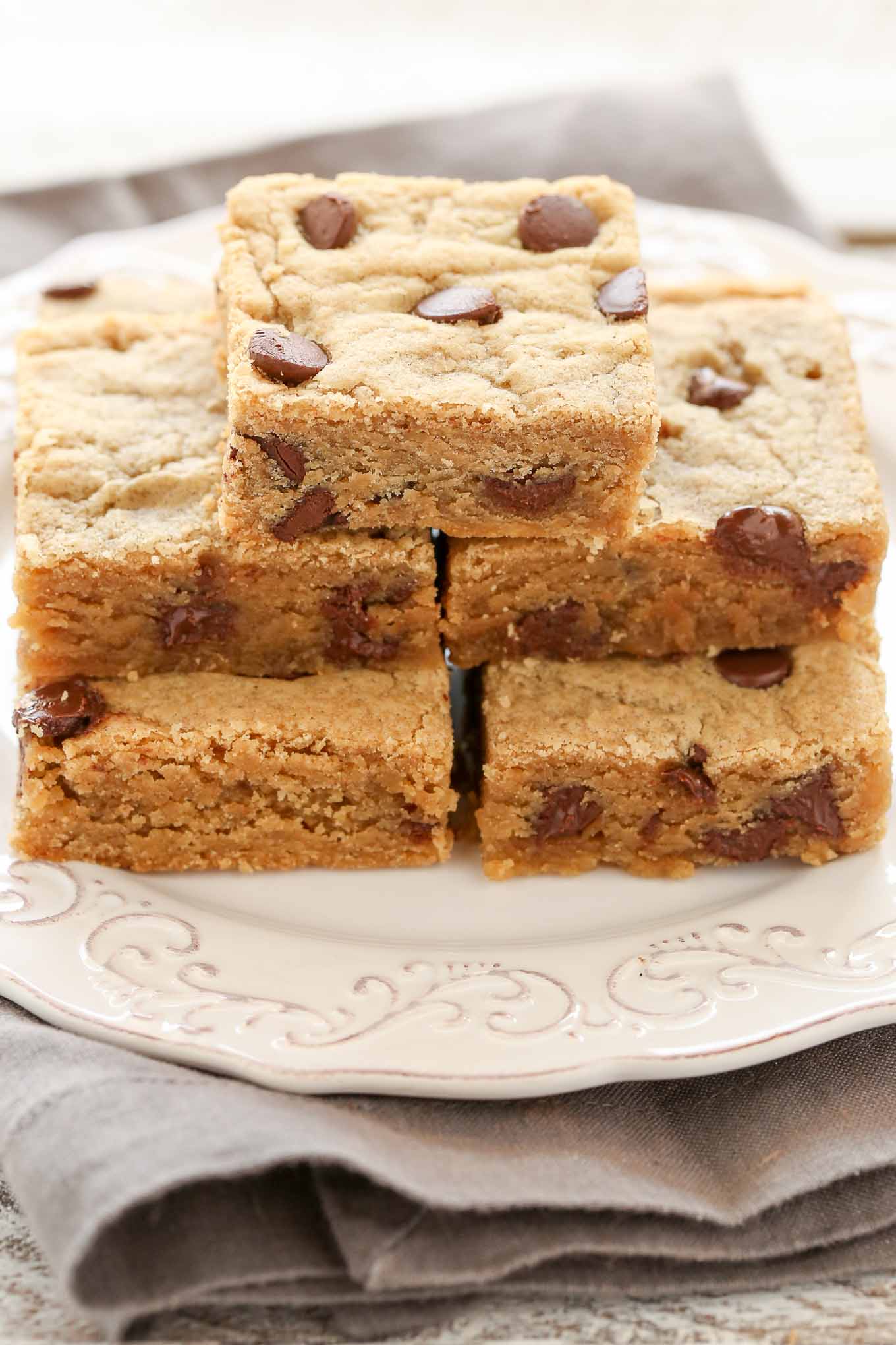 Five peanut butter chocolate chip bars stacked on a white plate. 