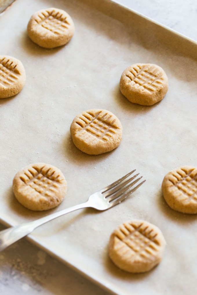 A baking sheet holding peanut butter balls pressed down with a fork to get the criss cross pattern.