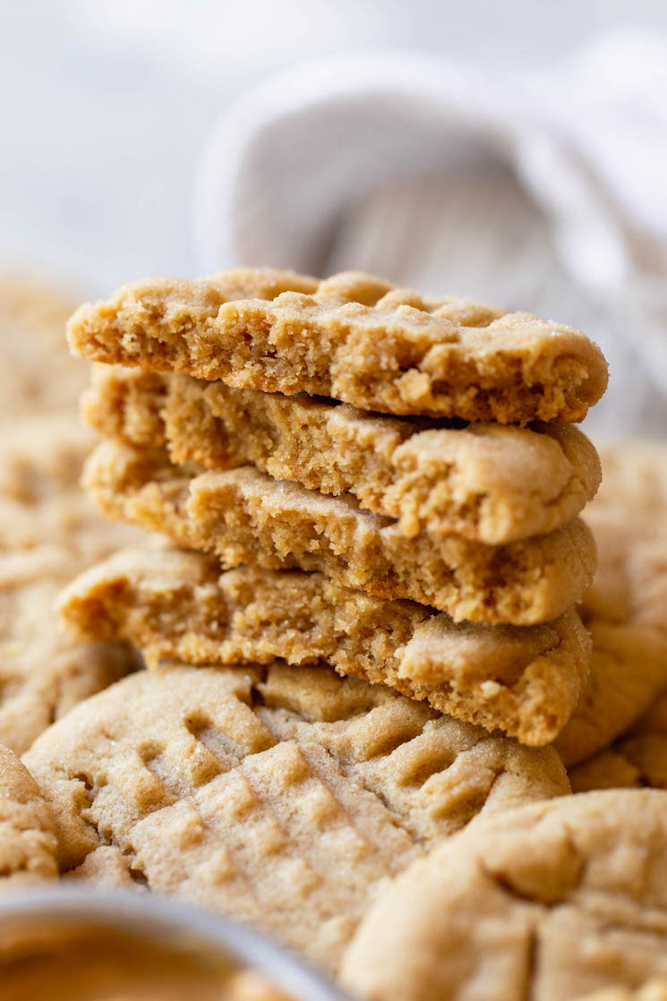 A stack of peanut butter cookies broken in half to show the texture on top of other cookies.
