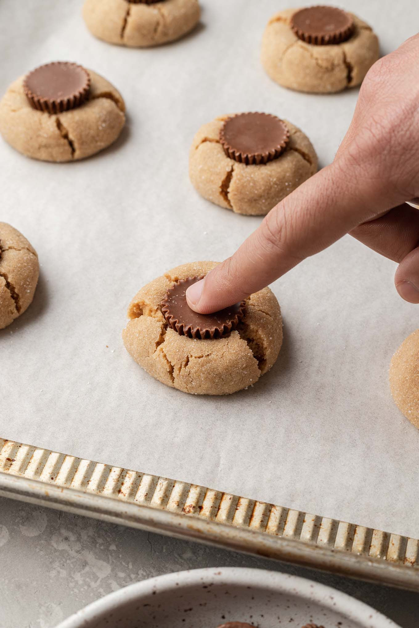 Mini peanut butter cups being pressed into baked peanut butter cookies. 