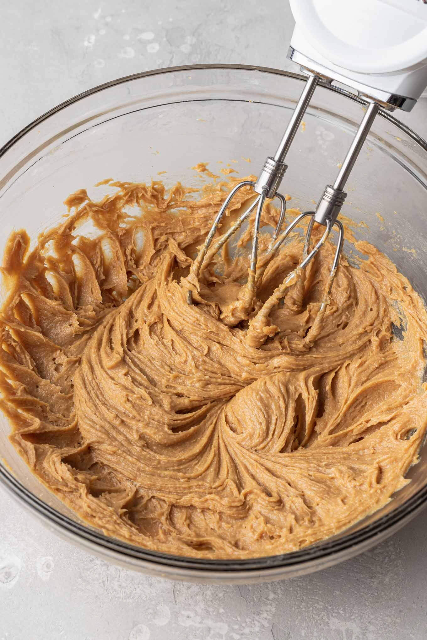 The wet ingredients for peanut butter cookie dough in a glass mixing bowl, with an electric beater. 