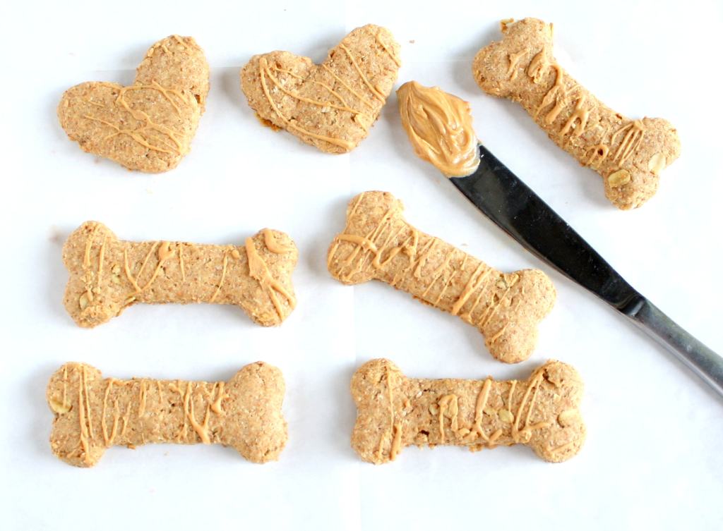 Overhead view of homemade peanut butter dog treats in various shapes. A knife with peanut butter on it rests in the middle. 